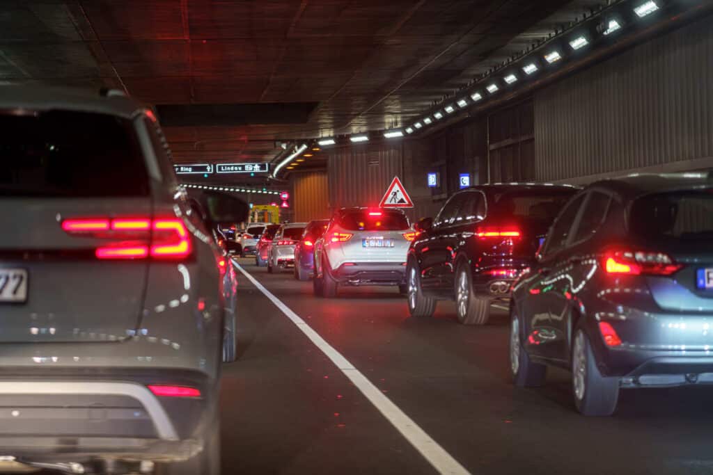 Trafic en Tunnel: Voitures à l'Arrêt, Feux Rouges Trafic dense et freinage dans un tunnel sombre avec feux arrière rouges allumés; panneaux indiquant Lindau 96.